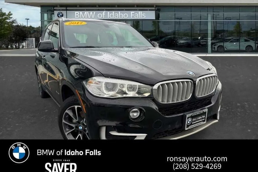 Black BMW X5 in a dealer photo with a storefront behind it and a dealer banner across the bottom, before AutoLander