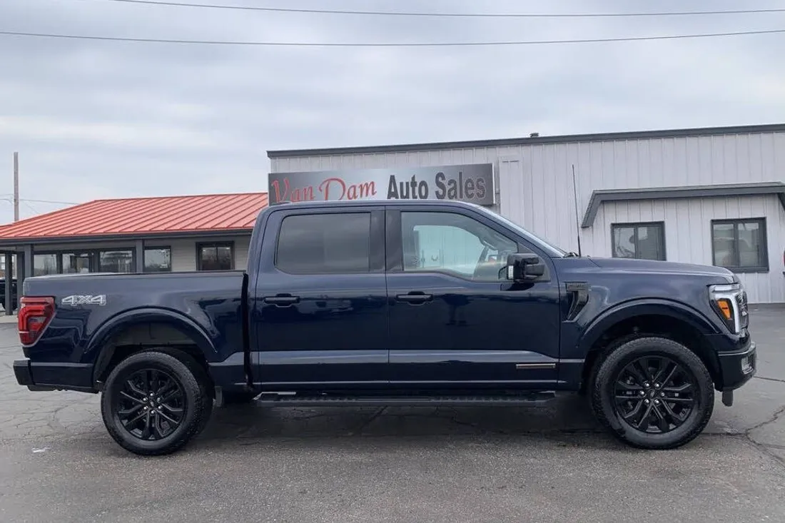 Dark blue Ford F-150 in a raw lot photo in front of a dealership building