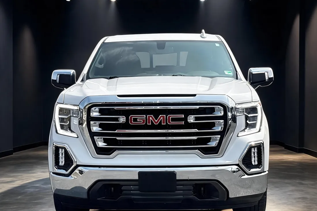 The same white frost tricoat 2022 GMC Sierra 1500 Limited SLT crew cab pickup in a straight-on front view, placed in a dark showroom scene by AutoLander's AI Photo Studio