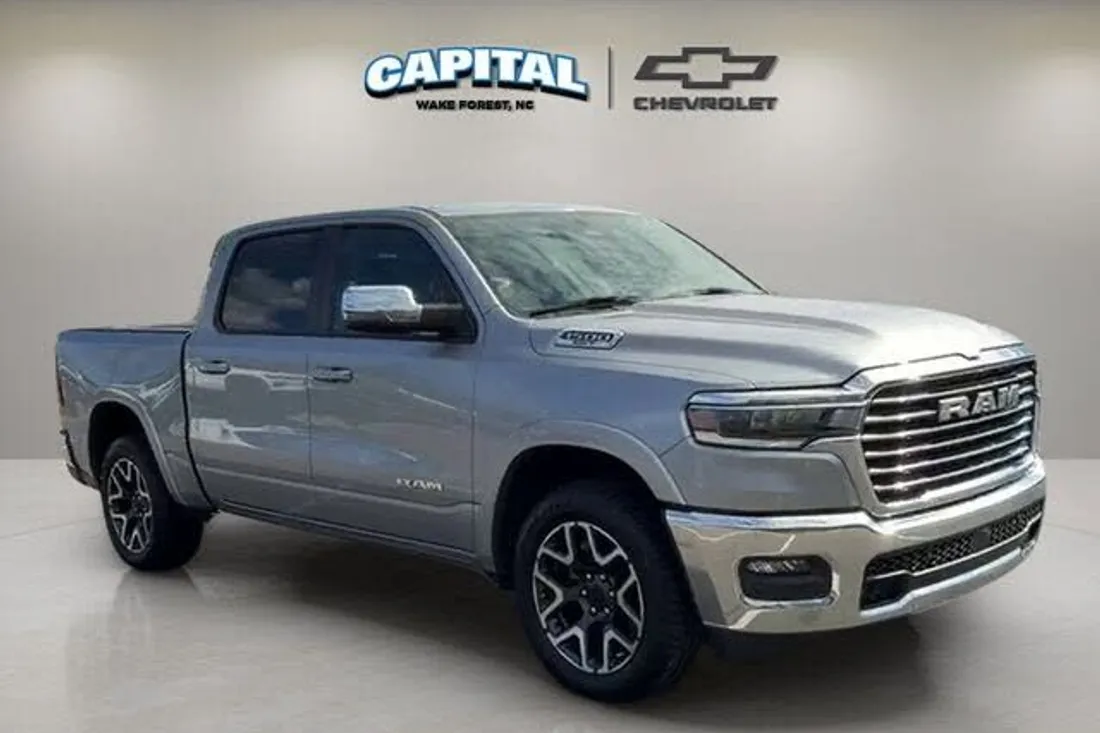 Silver RAM 1500 Laramie in a dealership showroom photo with the store logo on the wall, before AutoLander